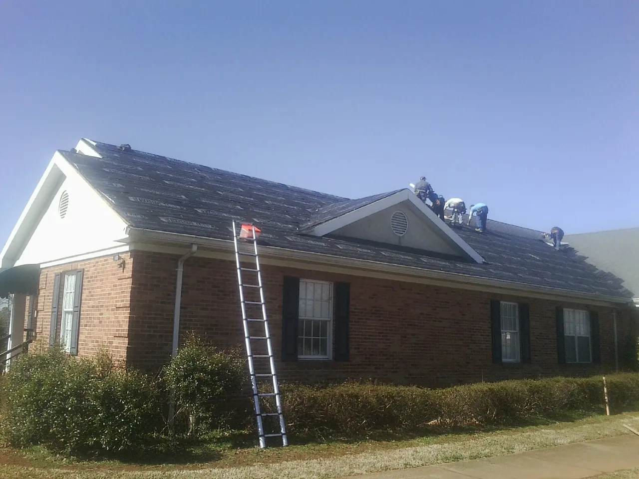Crew tearing shingles off a brick ranch roof with a ladder set — Metal Roof Repair work by our crew in Barboursville