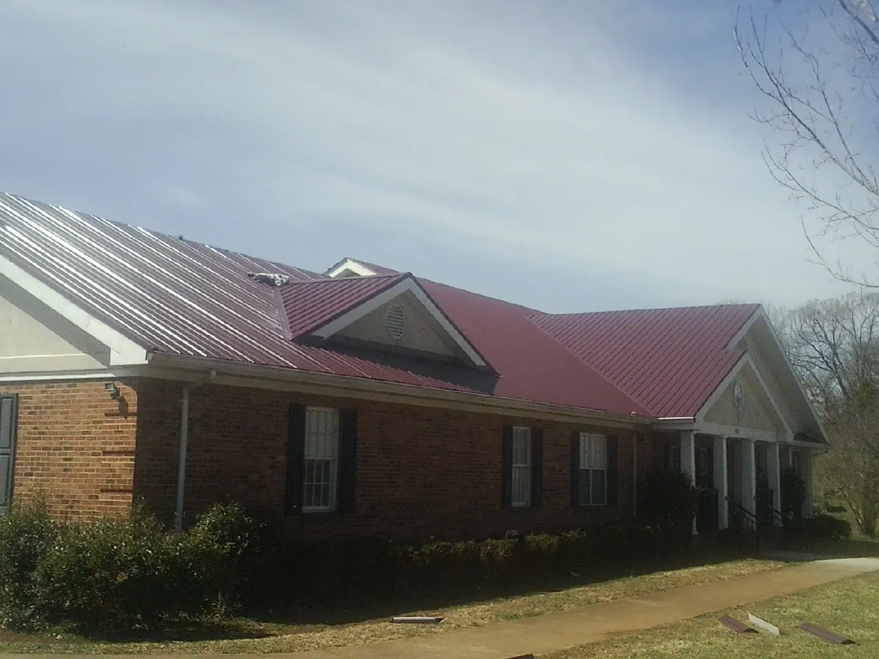 Red metal roof with gabled entries on a long brick building, from a Hail Damage Roof Repair job in Barboursville