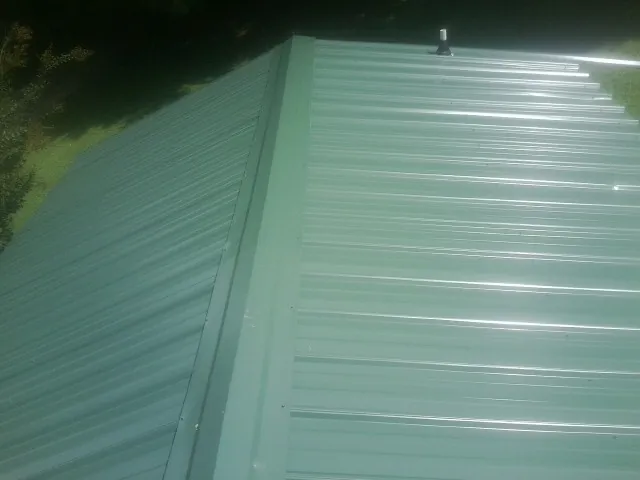New green metal panels meeting at the ridge of a roof — Flat Roof Repair work by our crew in Barboursville